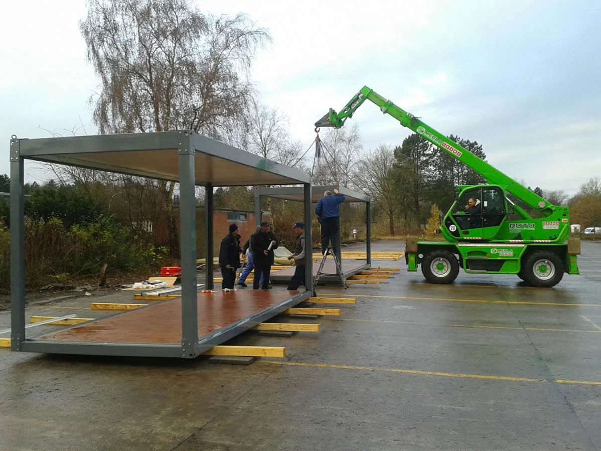 Assembly crew positioning the roof frame of a flat-pack module with a telehandler