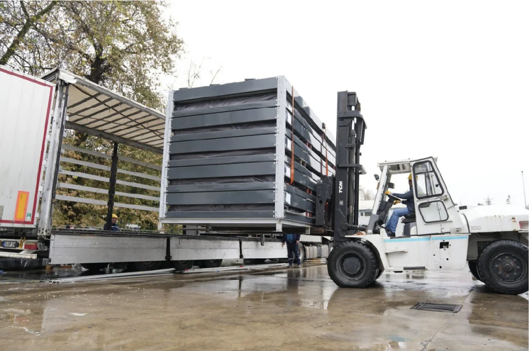 Forklift loading a stack of flat-pack container packages onto a curtain-side truck
