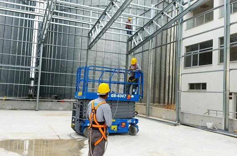 Assembly of warehouse roof framing with workers and an elevated work platform