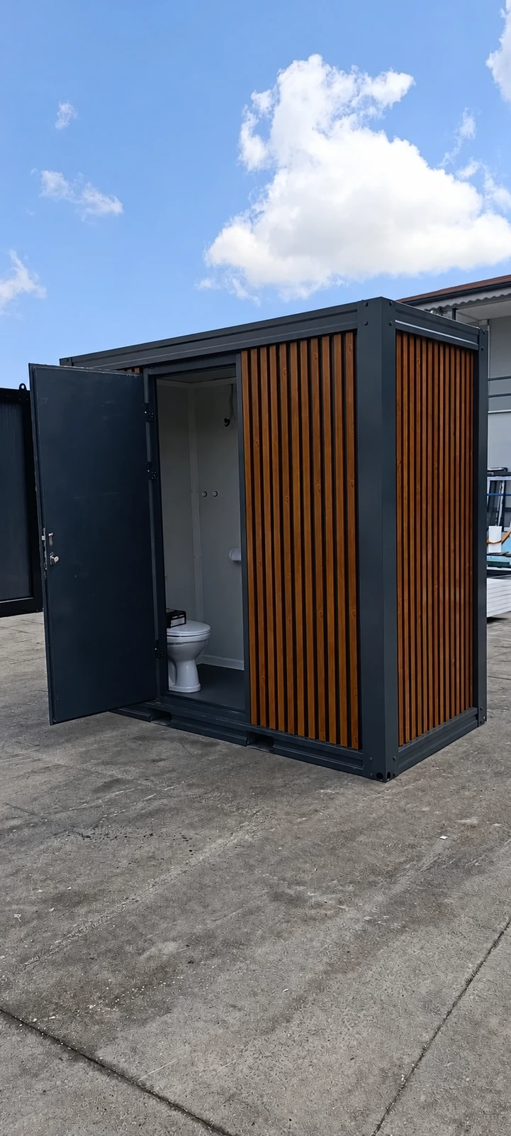 Compact sanitary cabin with dark frame, vertical exterior cladding and an open WC entrance