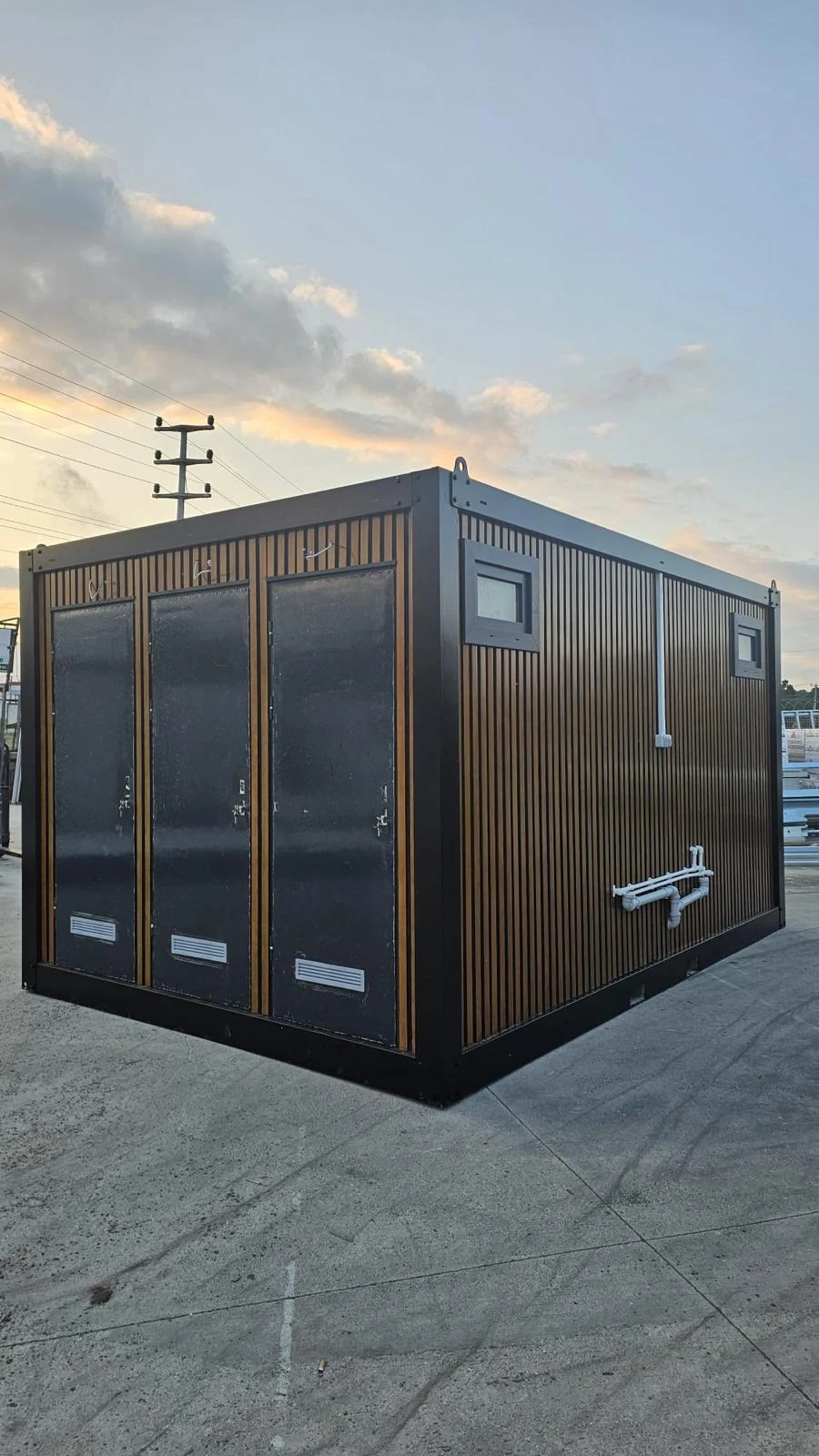 Sanitary container with dark frame, vertical exterior cladding, separate entrance doors and external plumbing