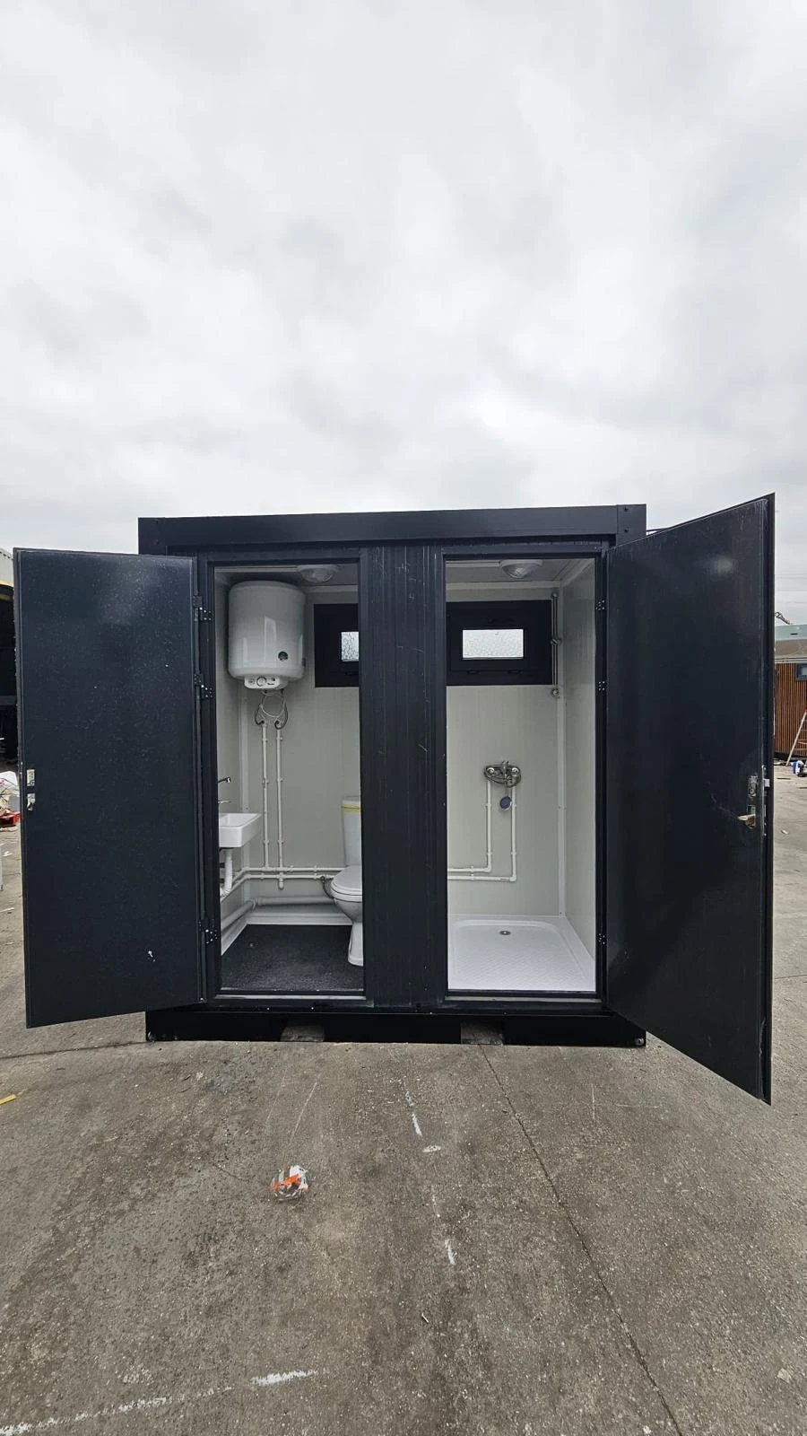 Open exterior doors revealing separate WC and shower compartments in a dark-framed sanitary unit